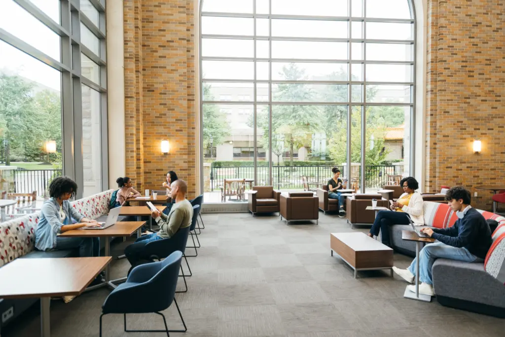Students focusing on studying or collaborating in a university library/multipurpose space.