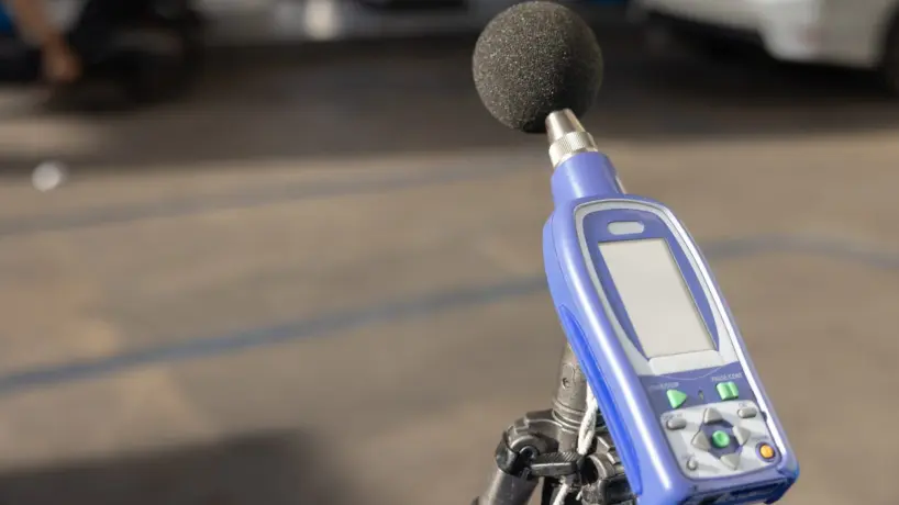 Acoustical consultant measuring sound levels after sound masking system installation in open office.