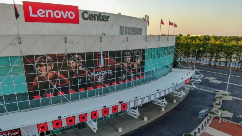 Low angle^ architectural detail shot looking up at the front entrance of the Lenovo Center. The glass facade of the arena is covered in large-scale promotional branding for the 2026 Stanley Cup Playoffs Eastern Conference Finals matchup between the Carolina Hurricanes and Montreal Canadiens. Prominent window vinyls feature portraits of team captain Jordan Staal and alternate captains Sebastian Aho and Jaccob Slavin alongside corporate venue logos^ captured under clear evening conditions ahead of the playoff series in North Carolina. Raleigh^ NC^ USA - May 19^ 2026