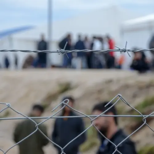 Barbed wire in refugee camp. Migrants behind chain link fence in camp. Group of people behind fence. Concept of prison^ freedom^ barrier^ security and migration. Refugees on their way to EU.