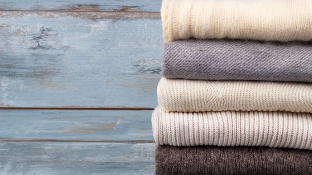 stack-of-white-and-gray-cozy-knitted-sweaters-on-rustic-wooden-background