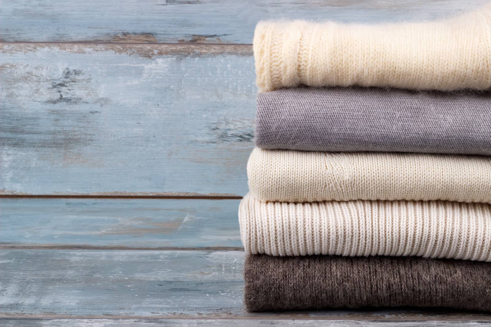 stack-of-white-and-gray-cozy-knitted-sweaters-on-rustic-wooden-background