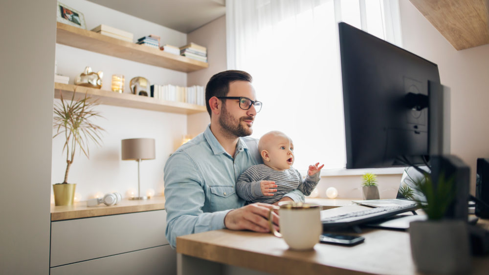 youngparentworkingfromhomewhileholdinghisbabyboy