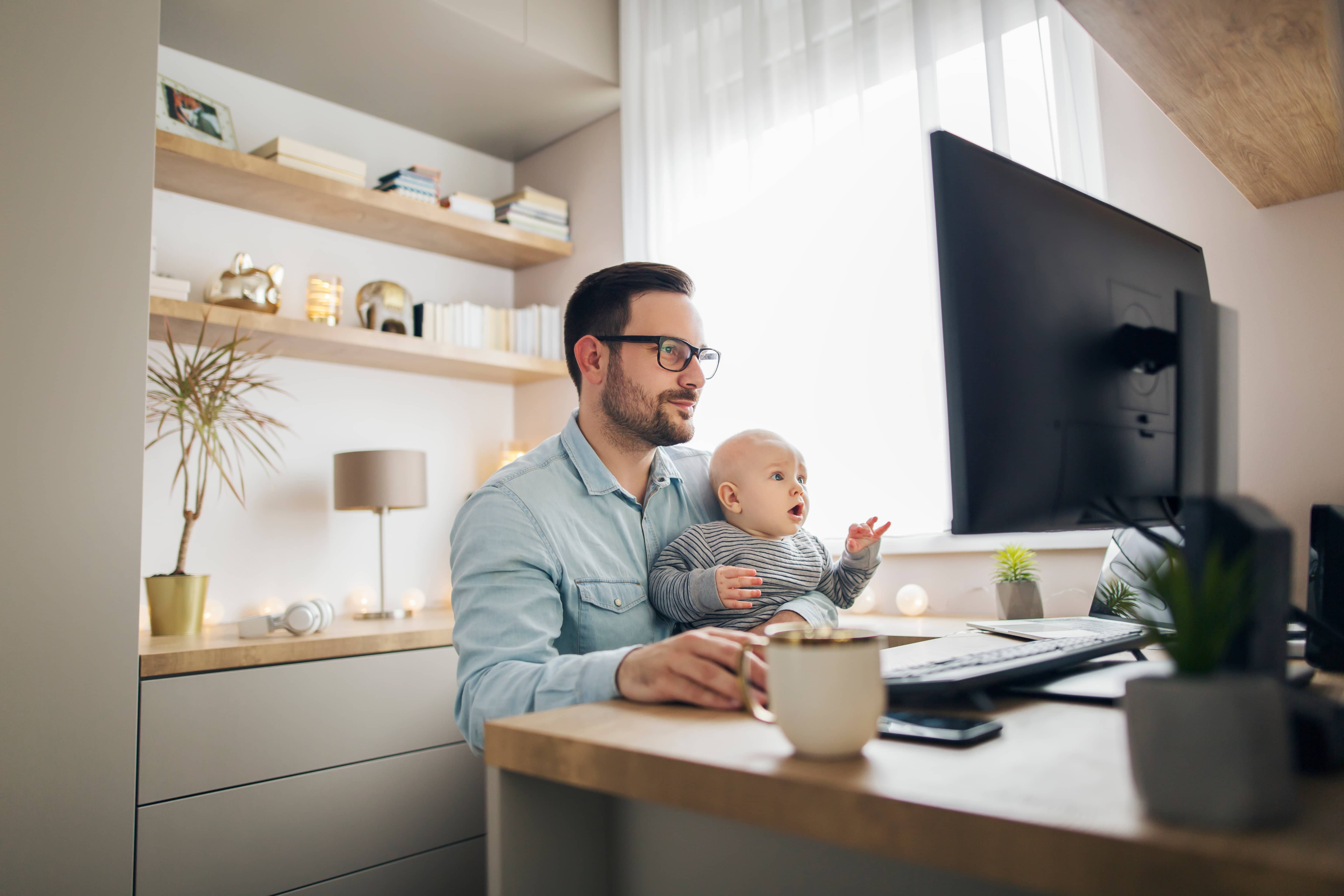 youngparentworkingfromhomewhileholdinghisbabyboy