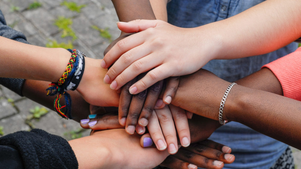 multiracial-teen-friends-joining-hands-together-in-cooperation