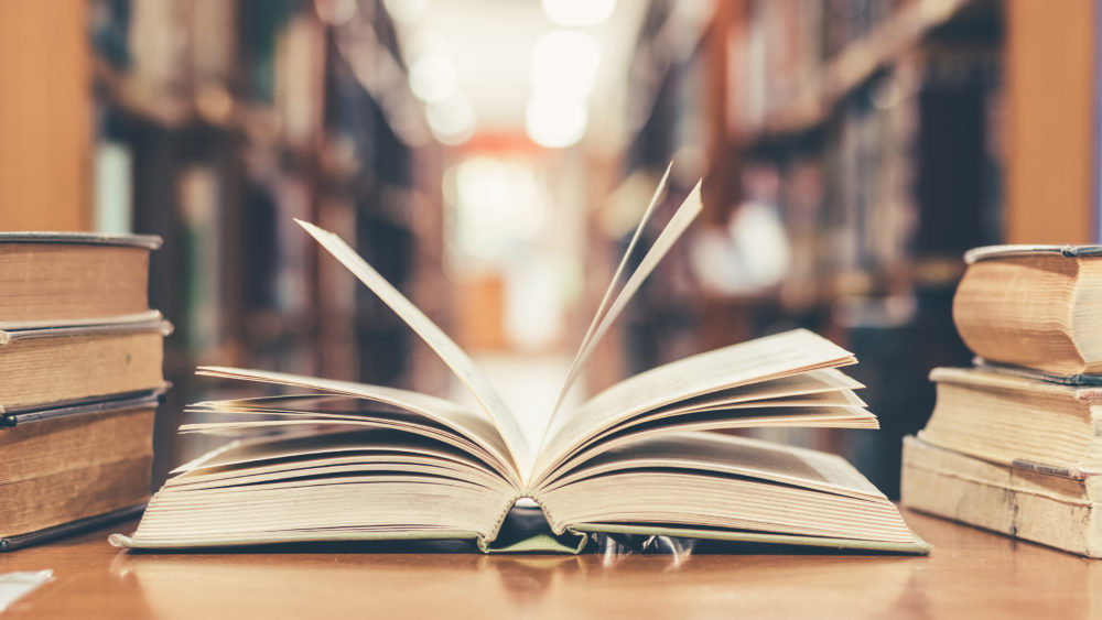 bookinlibrarywitholdopentextbookstackpilesof