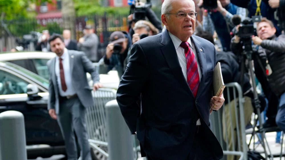 New Jersey Senator Bob Menendez walks towards courthouse with crowd of photographers in the background.