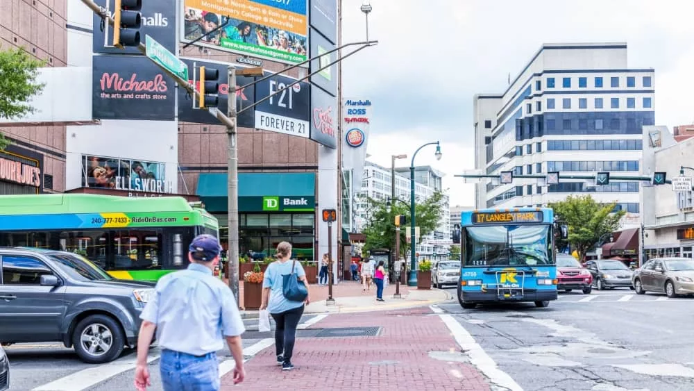 Downtown area of city in Maryland with cars on street^ bus^ and shopping mall stores^ shops and people.