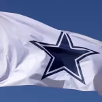 Dallas Cowboys flag flies in front of the AT&T Stadium located in Arlington^ Texas on March 14^ 2014. AT&T Stadium is home to the Dallas Cowboys of the NFL.