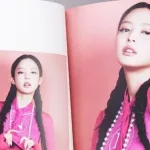 Fan hands holding BlackPink BORN PINK 2nd Album photobook with Jennie on grey. Pink music CD in player. South Korean girl group BlackPink