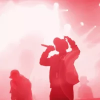 Silhouette of rap band performing on concert stage in bright red lights. Unrecognizable young rapper singing on concert