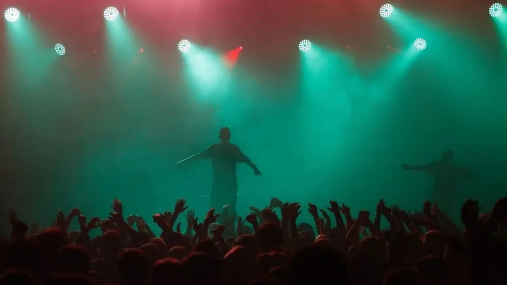 Rap singer performing on concert in music hall. Silhouette of rapper singing on stage in night club. Popuar hip hop music festival. Crowd of fans partying on dance floor