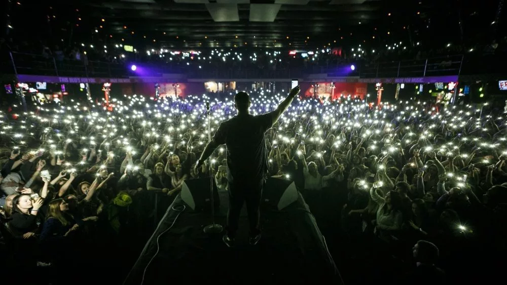 Concert wallpaper. Background with silhouette of rap singer on stage surrounded with fans.