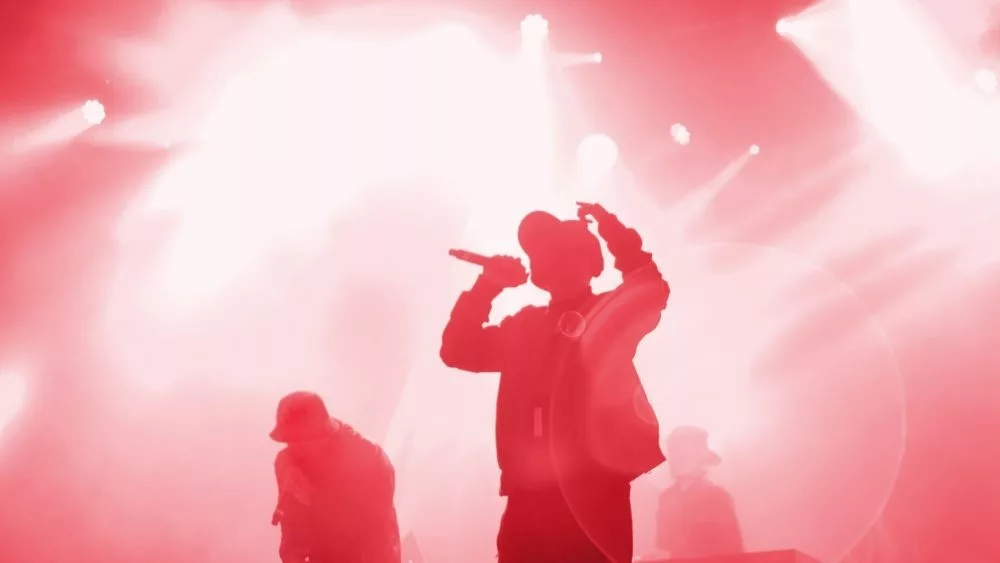 Silhouette of rap band performing on concert stage in bright red lights. Unrecognizable young rapper singing on concert
