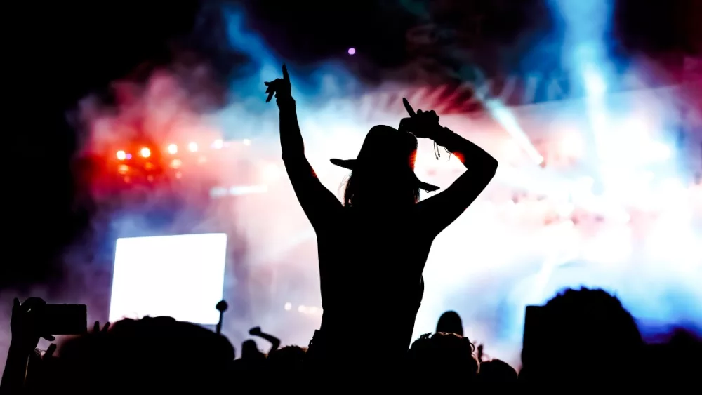 femela concertgoer in silhouette in front of stage lights^ watching show