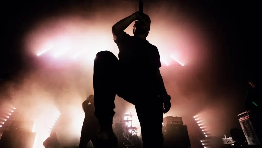 A dark silhouette of a singer on the stage. background^ bright stag lights.