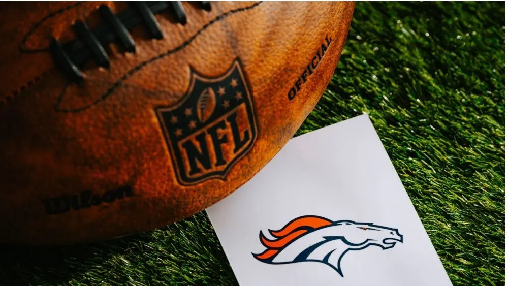 Denver Broncos NFL team Logo and American football ball on Green Grass.