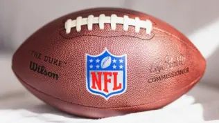 NFL Wilson Duke ball over a white sofa in a home. Sun light comes from a window.