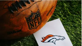 Denver Broncos NFL team Logo and American football ball on Green Grass.