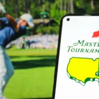 Masters Tournament logo displayed on a mobile phone with a photo of a player taking a swing on its website in the background^ the world's premier golf championship. Indonesia - May 15^ 2025