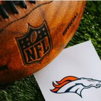 Denver Broncos NFL team Logo and American football ball on Green Grass.