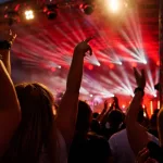 Silhouettes of crowd at concert in front of stage with bright spotlights. People enjoy live music at the band's performance. Concert hall with musicians on stage and fans during music festival