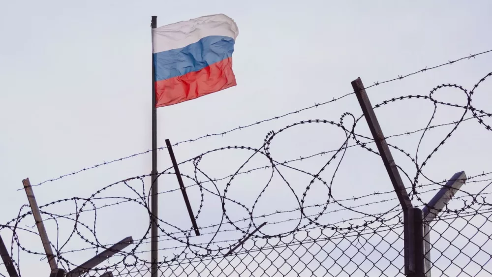 View of russian flag behind barbed wire against cloudy sky. Concept anti-Russian sanctions. A border post on the border of Russia. cancel culture Russia in the world