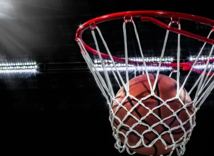 Looking up at an orange basketball falling through the rim and a white nylon net. With the arena lights in the background.