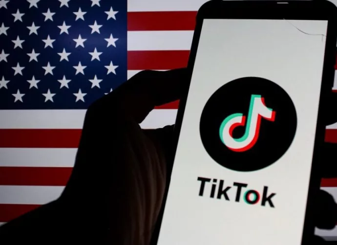 Photo illustration of TikTok logo displayed on a smartphone with American Flag in the background.