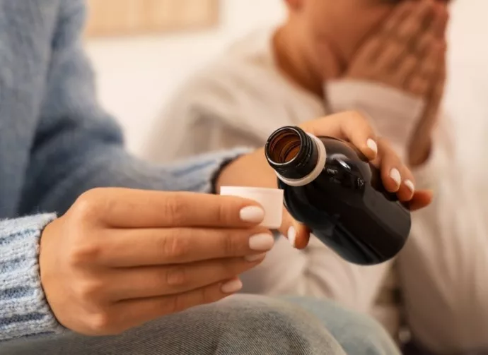 Mother giving cough syrup to her sick son in bed