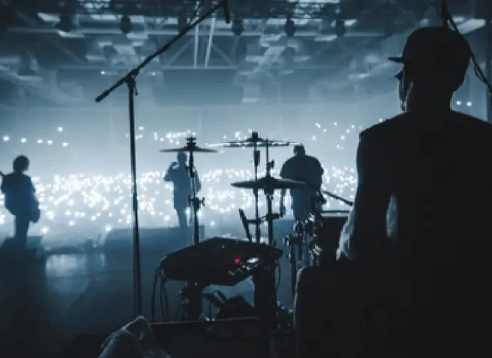 rock band viewed from behind the stage performing to sold-out audience; view of drummers^ guitarists in silhouette in hazy photo