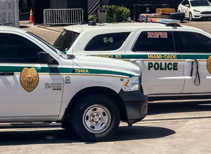 Two Miami-Dade police K-9 cars are parked near a metal security fence on a bright sunny day. Miami^ Florida^ USA^ June 16th 2025