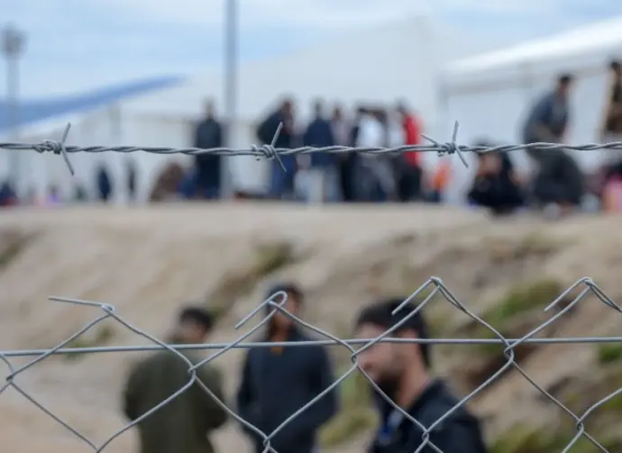 Barbed wire in refugee camp. Migrants behind chain link fence in camp. Group of people behind fence. Concept of prison^ freedom^ barrier^ security and migration. Refugees on their way to EU.