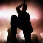A dark silhouette of a singer on the stage. background^ bright stag lights.