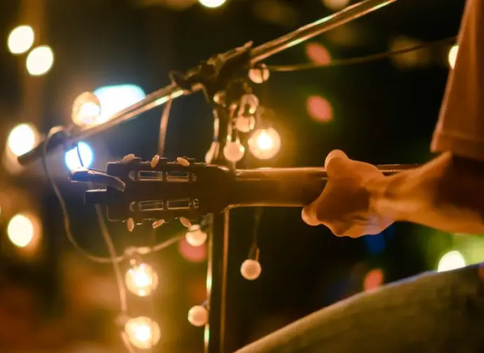 Rear view of the man sitting play acoustic guitar on the outdoor concert with a microphone stand in the front^ musical concept.