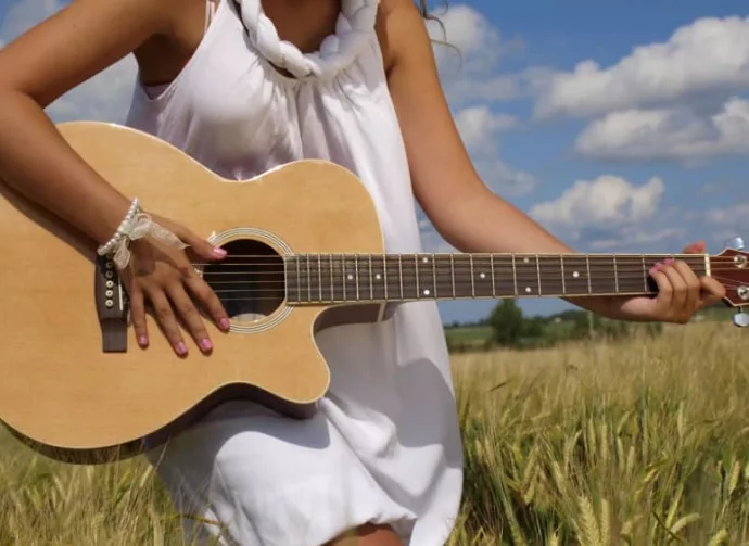 woman in field playing guitar in white dress