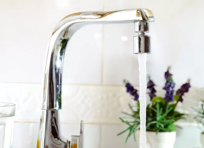 Open kitchen sink faucet flowing stream of water purified by domestic reverse osmosis with filters around. Front view. Horizontal composition.