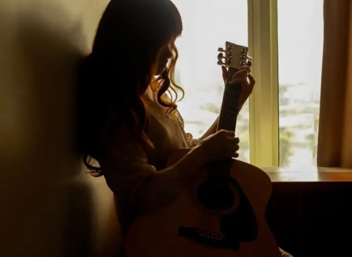 Silhouette of a young woman playing guitar alone in the dark