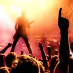 view from crowd cheering rock band performing on stage^ guitarist in silhouette
