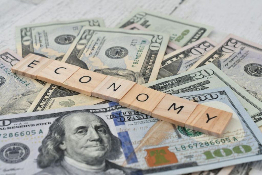 the-word-economy-spelled-out-in-wooden-letter-tiles-on-a-pile-of-cash-money-currency-1024x683-1