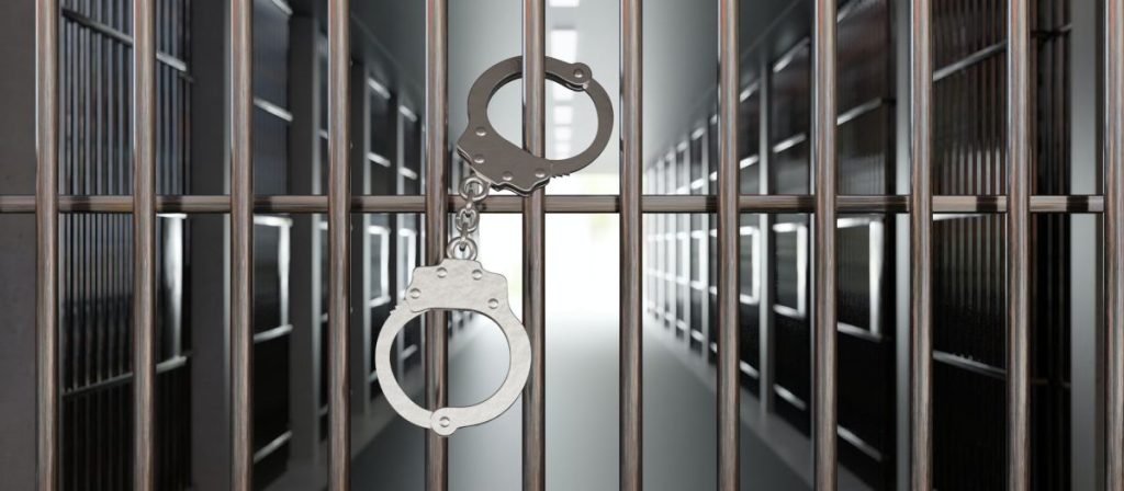 handcuffs-on-jail-cell-closed-metal-bar-door-prison-building-corridor-background-3d-render-1024x448-1