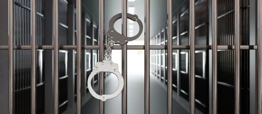 handcuffs-on-jail-cell-closed-metal-bar-door-prison-building-corridor-background-3d-render-1024x448490064-1