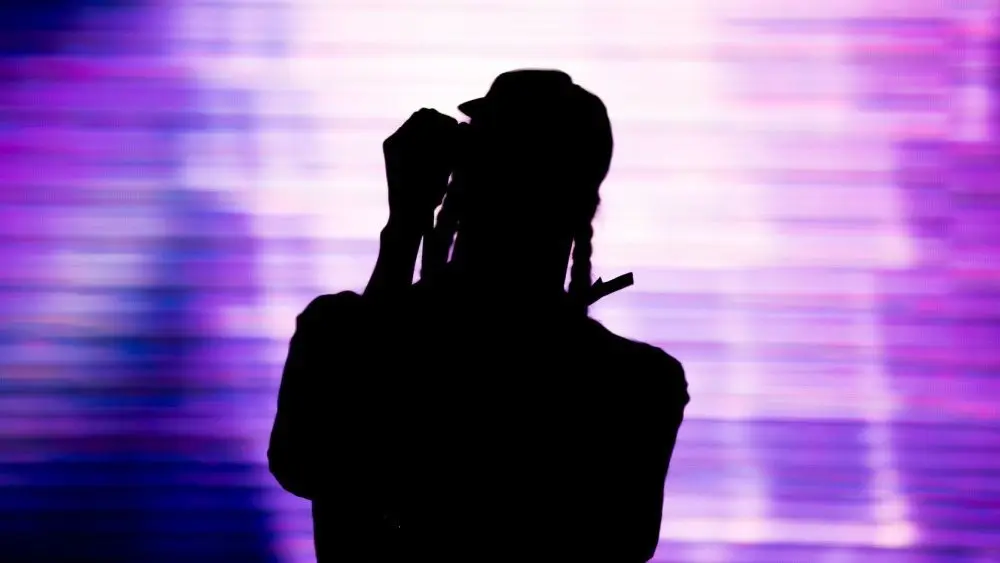 Silhouette of an artist singing live on the stage in the front of a colorful background