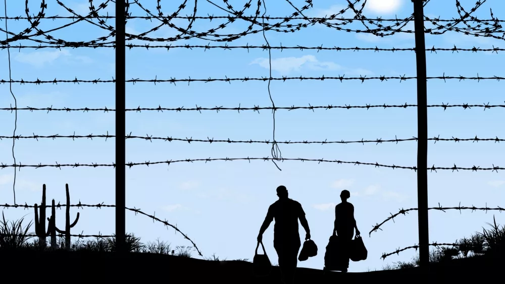 A man and woman in silhouette heading through broken border fence on the southern border of the USA.