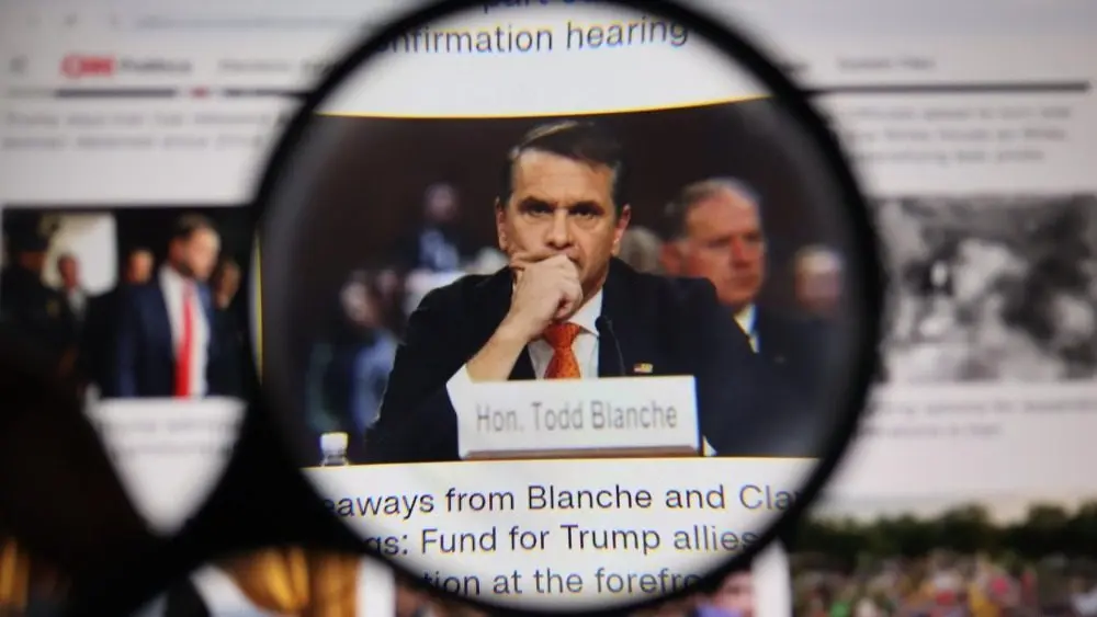 Close up through magnifying lens capturing legal professional Todd Blanche with nameplate at desk during hearing. Law and courtroom justice journalism concept.