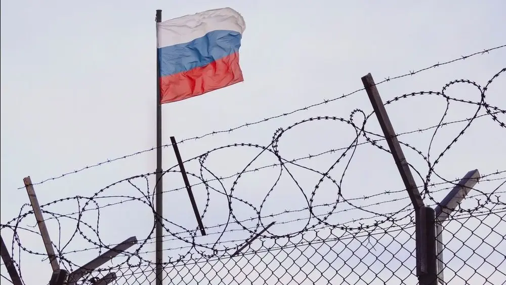 View of russian flag behind barbed wire against cloudy sky. Concept anti-Russian sanctions. A border post on the border of Russia.
