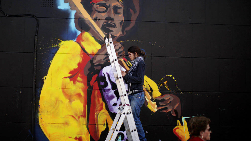 a-woman-paints-graffiti-of-the-rock-star-jimi-hendrix-on-the-wall-of-a-music-shop-in-malaga