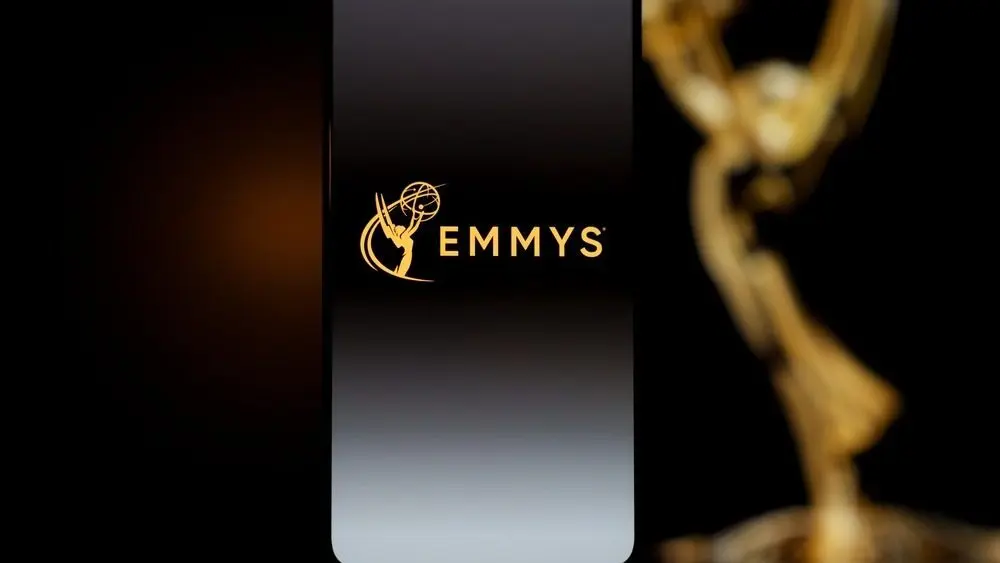 Emmys logo displayed on a smartphone screen with a blurred gold award statuette in the background^ television industry awards and digital streaming concept. Kaunas^ Lithuania - 2026 March 24