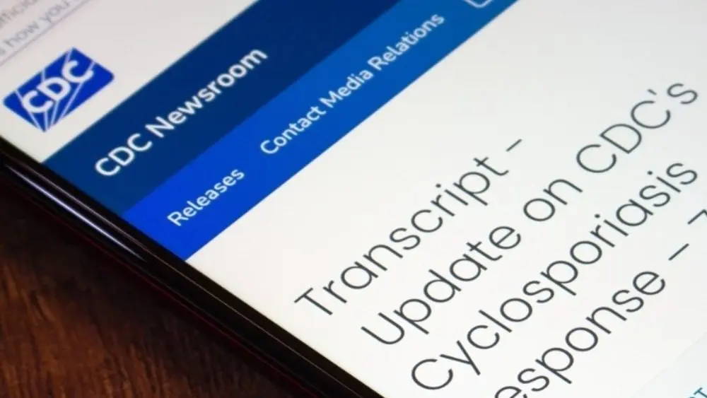 Mexico City^ MEXICO - Jul 21 2026 : Close-up of a smartphone on a wooden surface showing the CDC Newsroom webpage with a transcript titled Update on CDC's Cyclosporiasis Response.