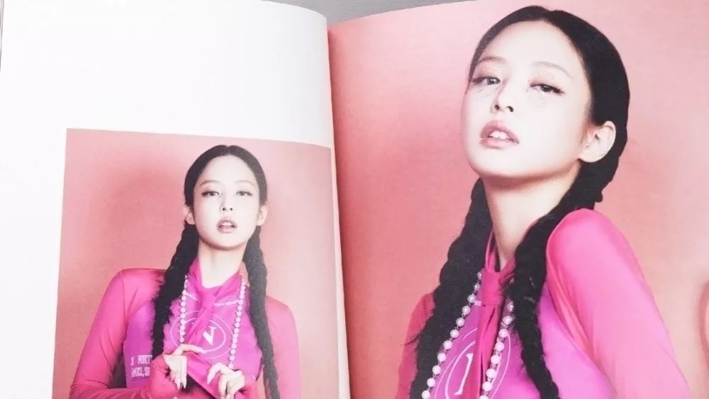 Fan hands holding BlackPink BORN PINK 2nd Album photobook with Jennie on grey. Pink music CD in player. South Korean girl group BlackPink